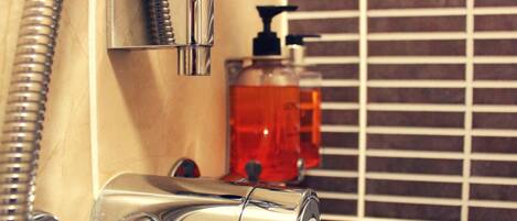 A bathroom with a chrome faucet, a soap dispenser, and a showerhead.