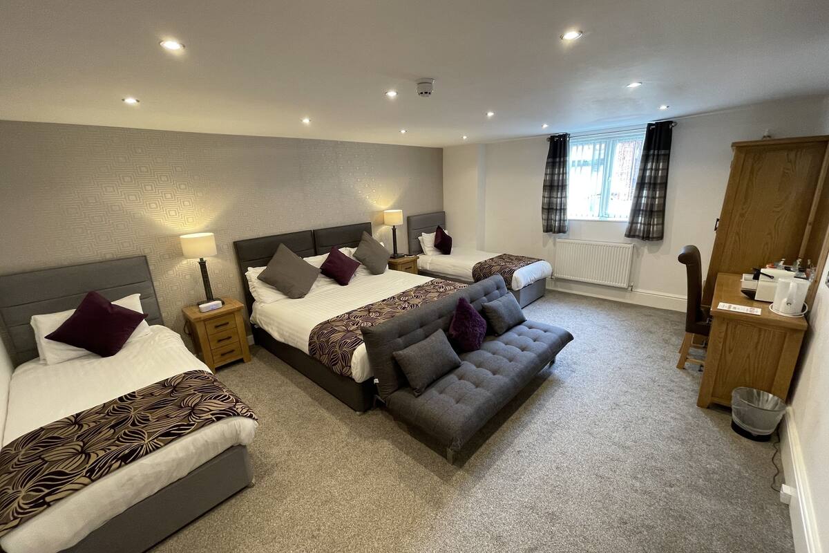 A hotel room with two beds, a sofa, a wooden nightstand, a radiator, and a window with curtains.