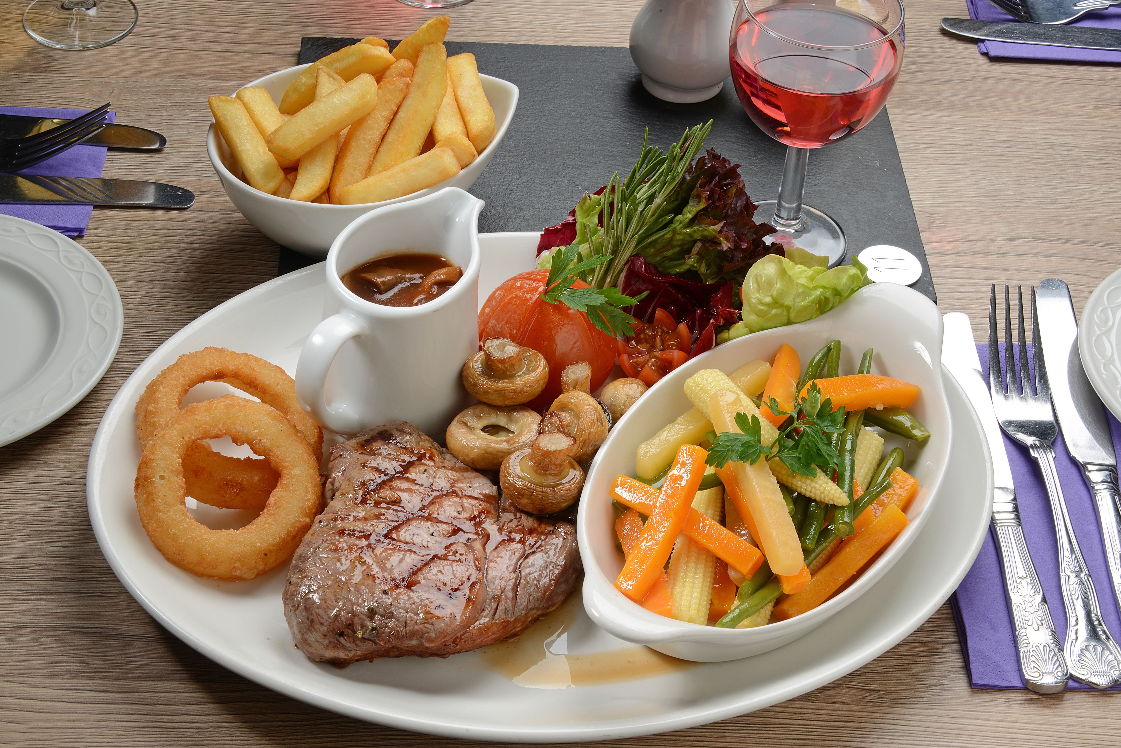 Een bord eten met steak, uienringen, frietjes en een kleine salade.