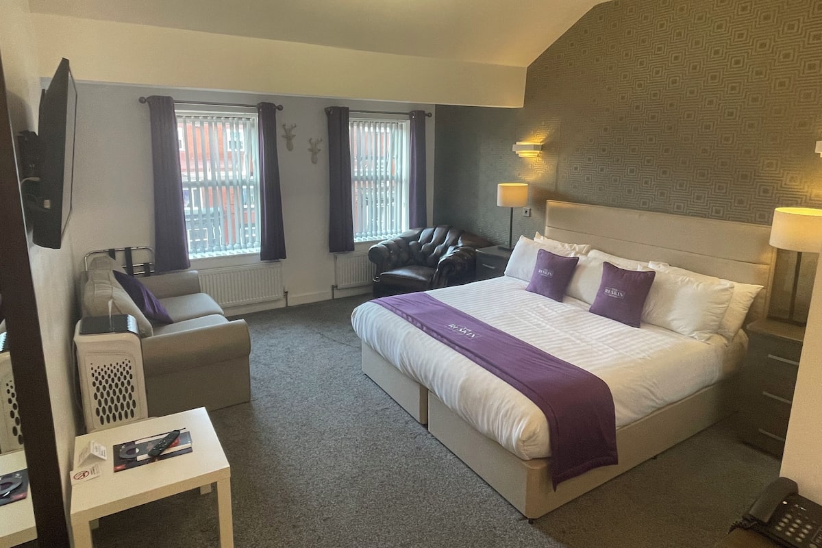 A hotel room with a large bed, a sofa, a TV, and a desk.