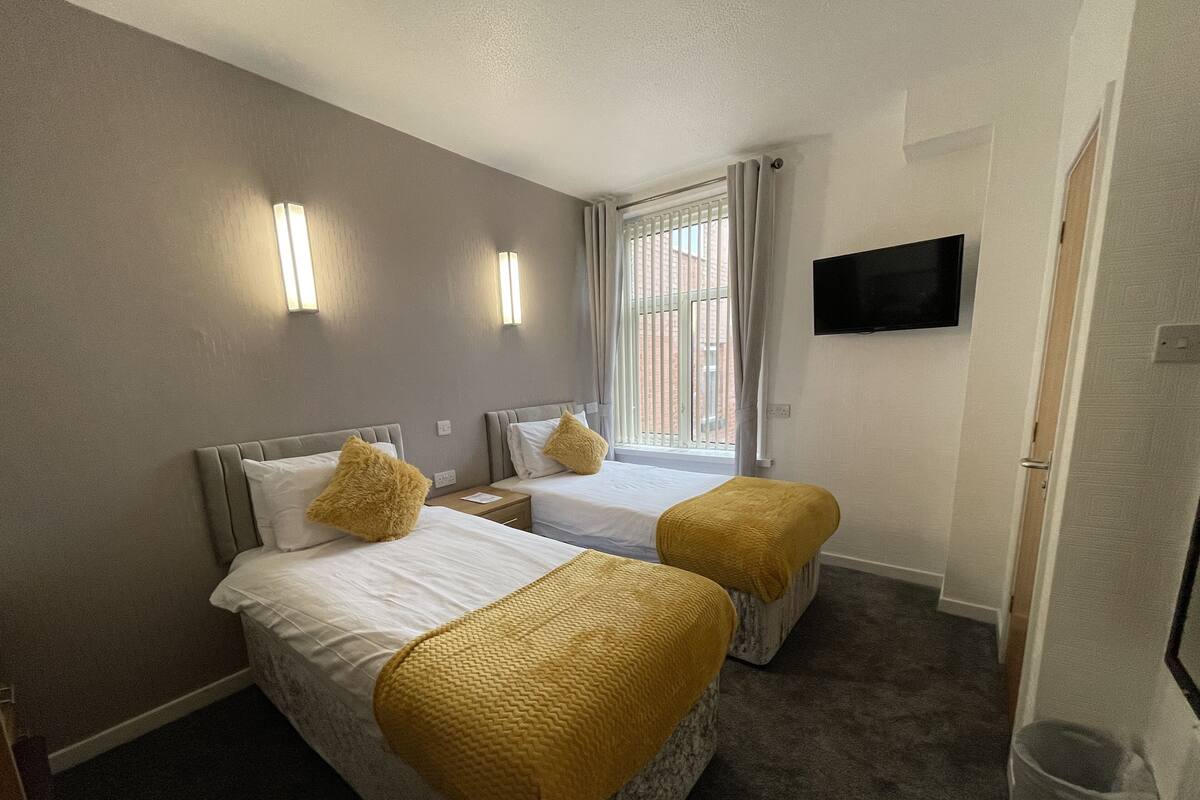 A hotel room with two beds, a TV, and a window with blinds.