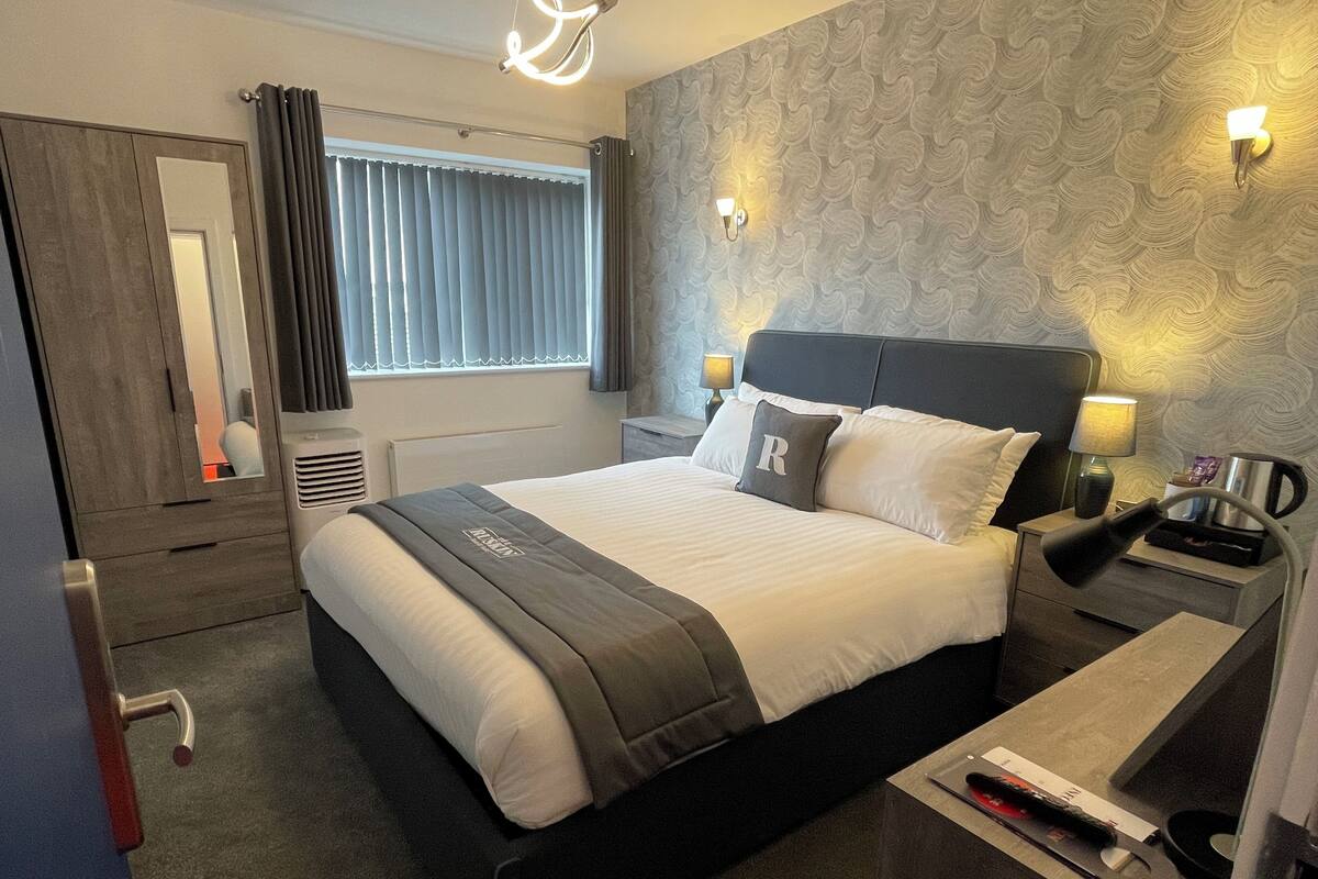 A hotel room with a large bed, bedside lamps, a nightstand, a mirror, and a window with curtains.