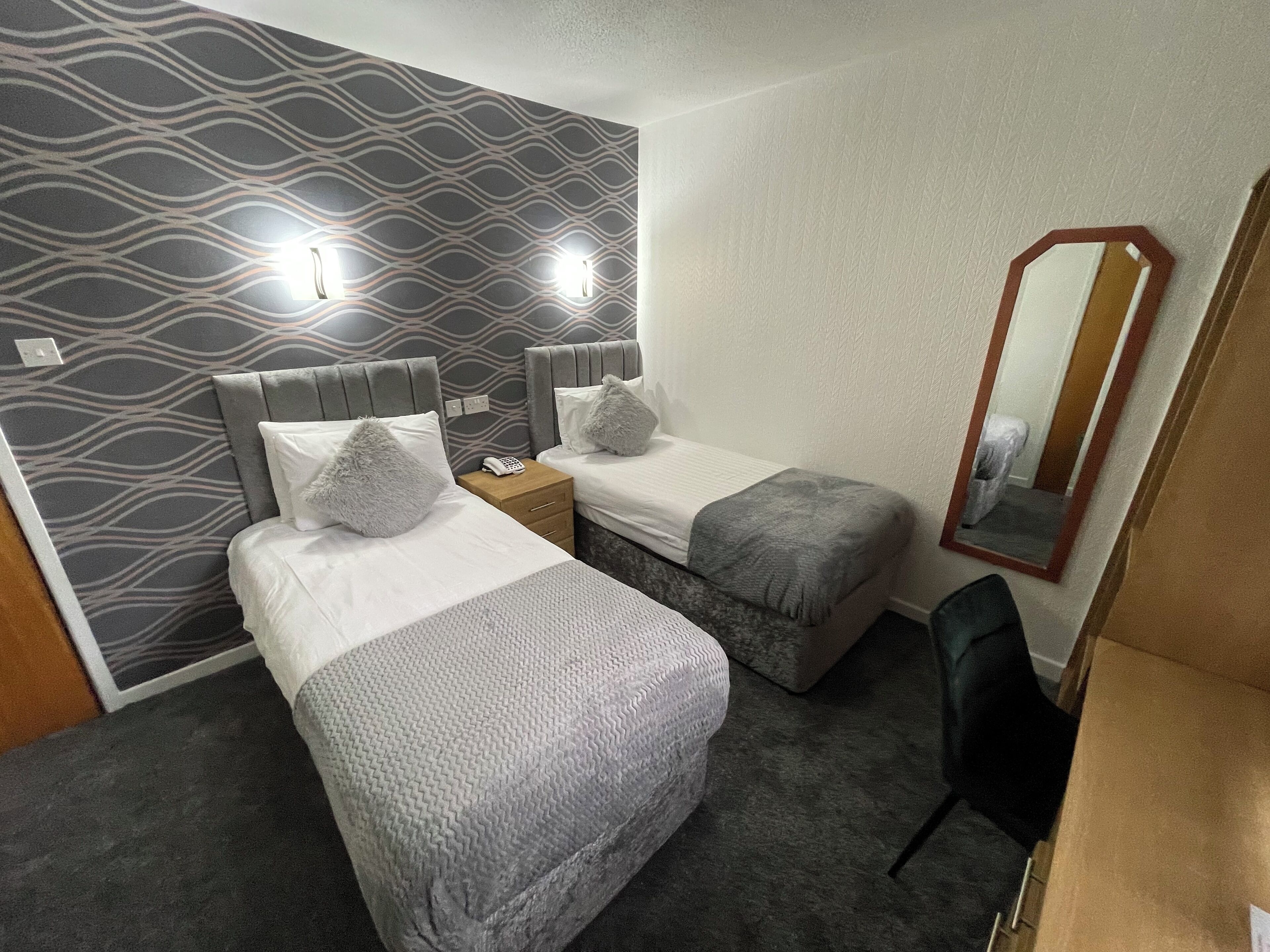 A hotel room with two beds, a small desk, a mirror, and a carpeted floor.
