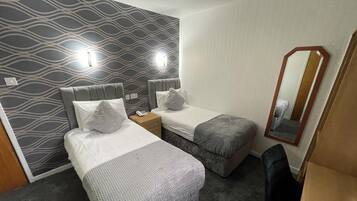 A hotel room with two beds, a small desk, a mirror, and a carpeted floor.