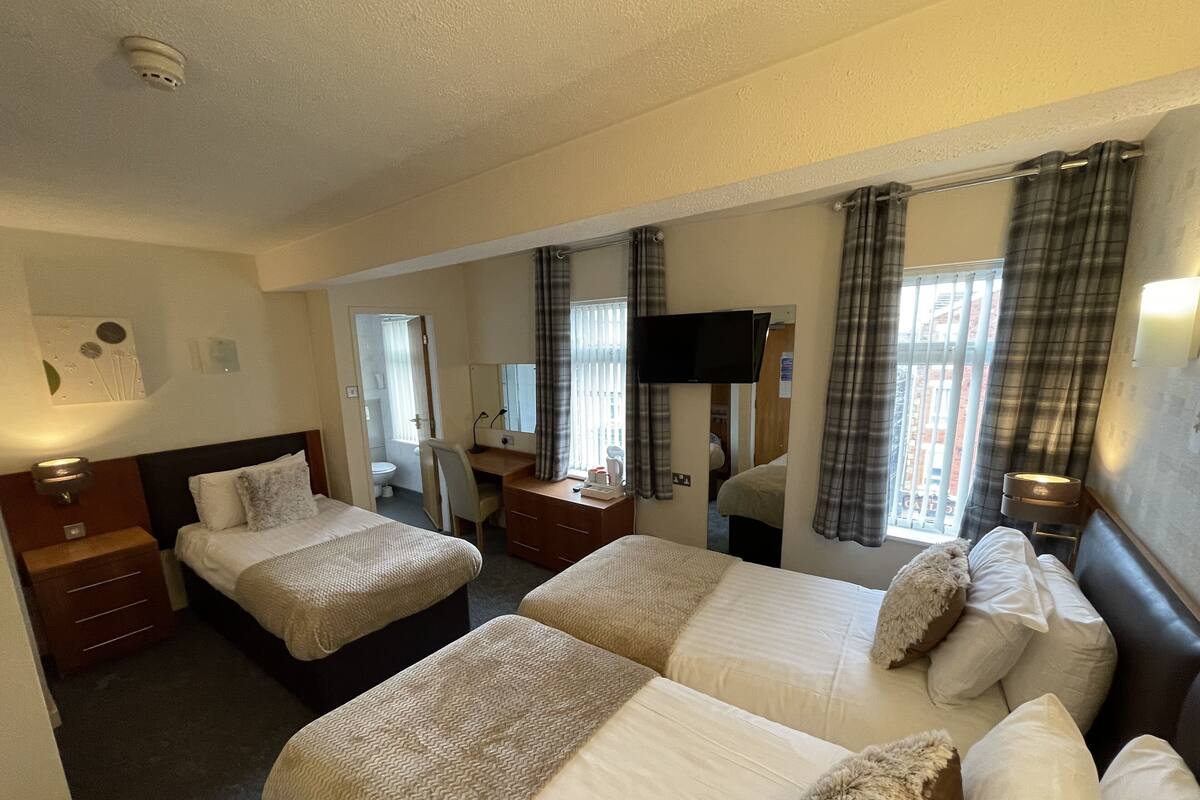 A hotel room with two beds, a desk, a chair, a TV, and a bathroom visible through an open door.