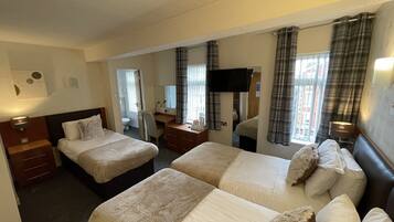 A hotel room with two beds, a desk, a chair, a TV, and a bathroom visible through an open door.