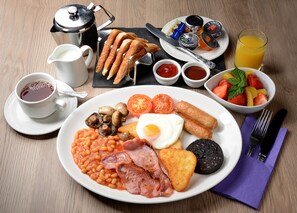 Un plato de desayuno con huevos, tocino, frijoles, tomates, champiñones, salchichas, tostadas y fruta como acompañamiento.