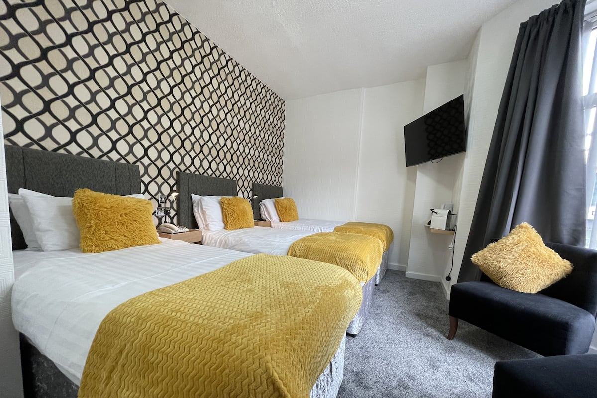 A hotel room with two beds, a sofa, a TV, and a patterned wall.