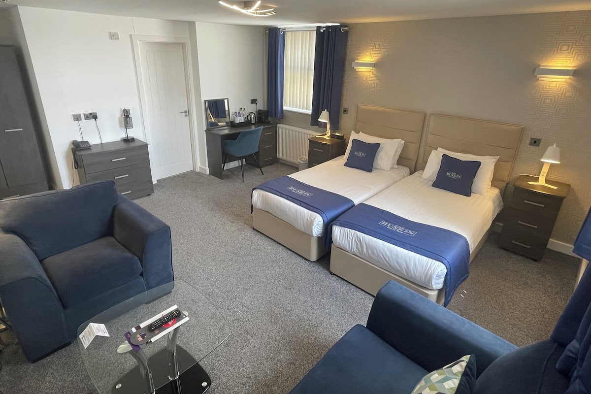 A hotel room with two beds, a desk, a chair, and a sofa.