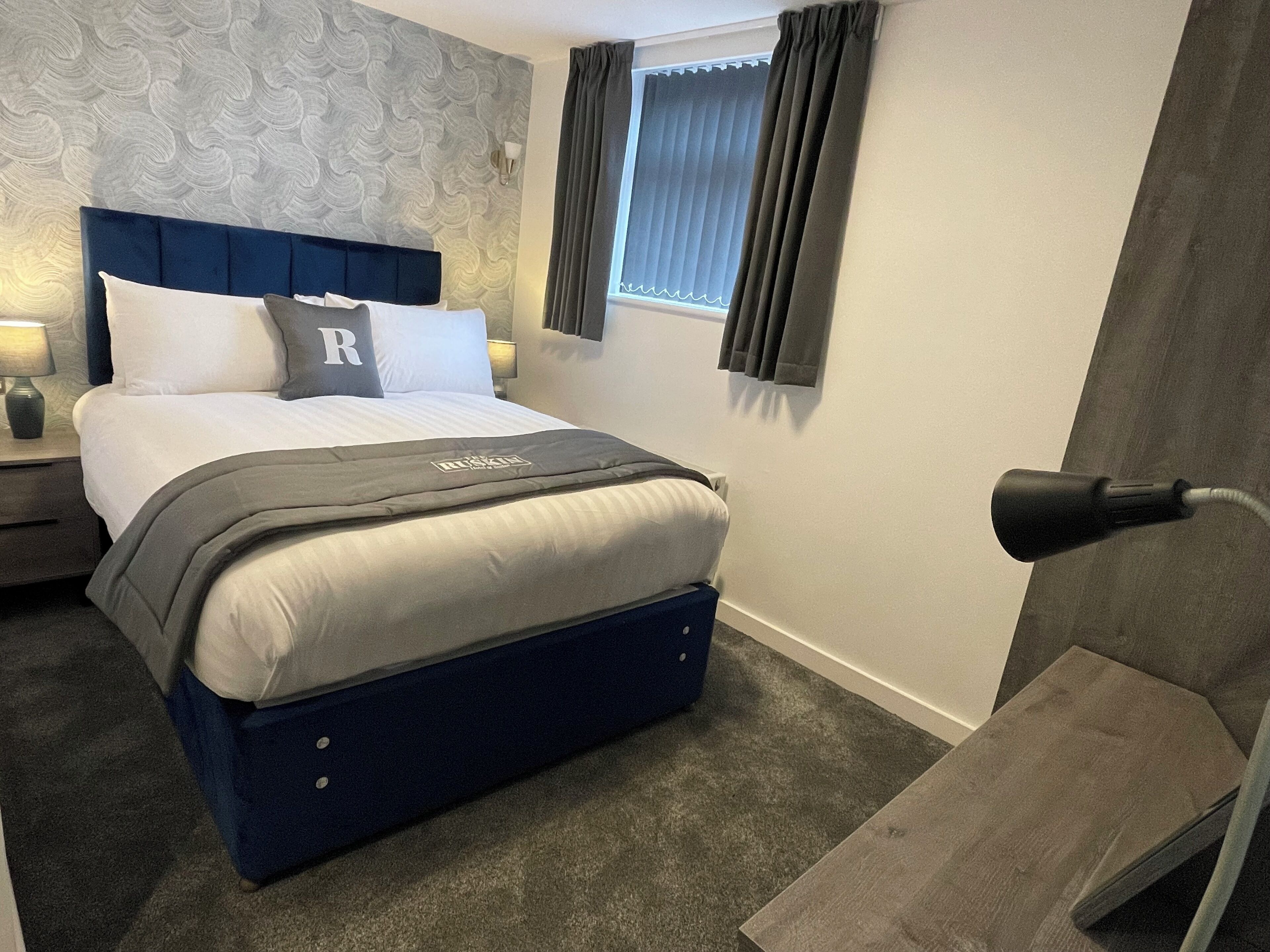 A neatly arranged bedroom with a bed, a bedside table, a lamp, and a window with curtains.