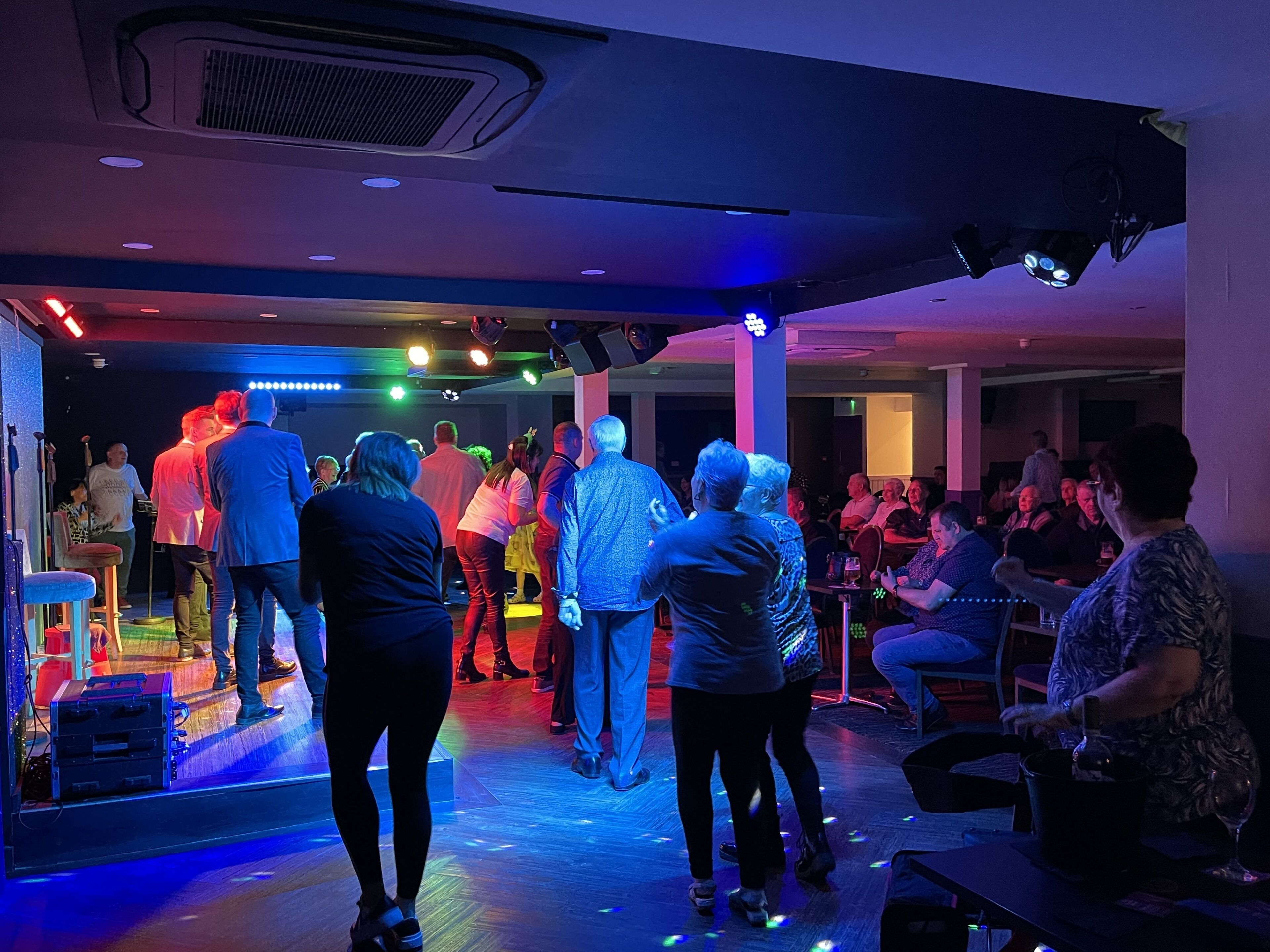 Een drukke binnenruimte met een podium, zitgedeelte en een bar.