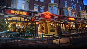 A hotel with a prominent 'RUSKIN' sign, a well-lit entrance, and a staircase leading to the entrance. - Ruskin Hotel (Blackpool)