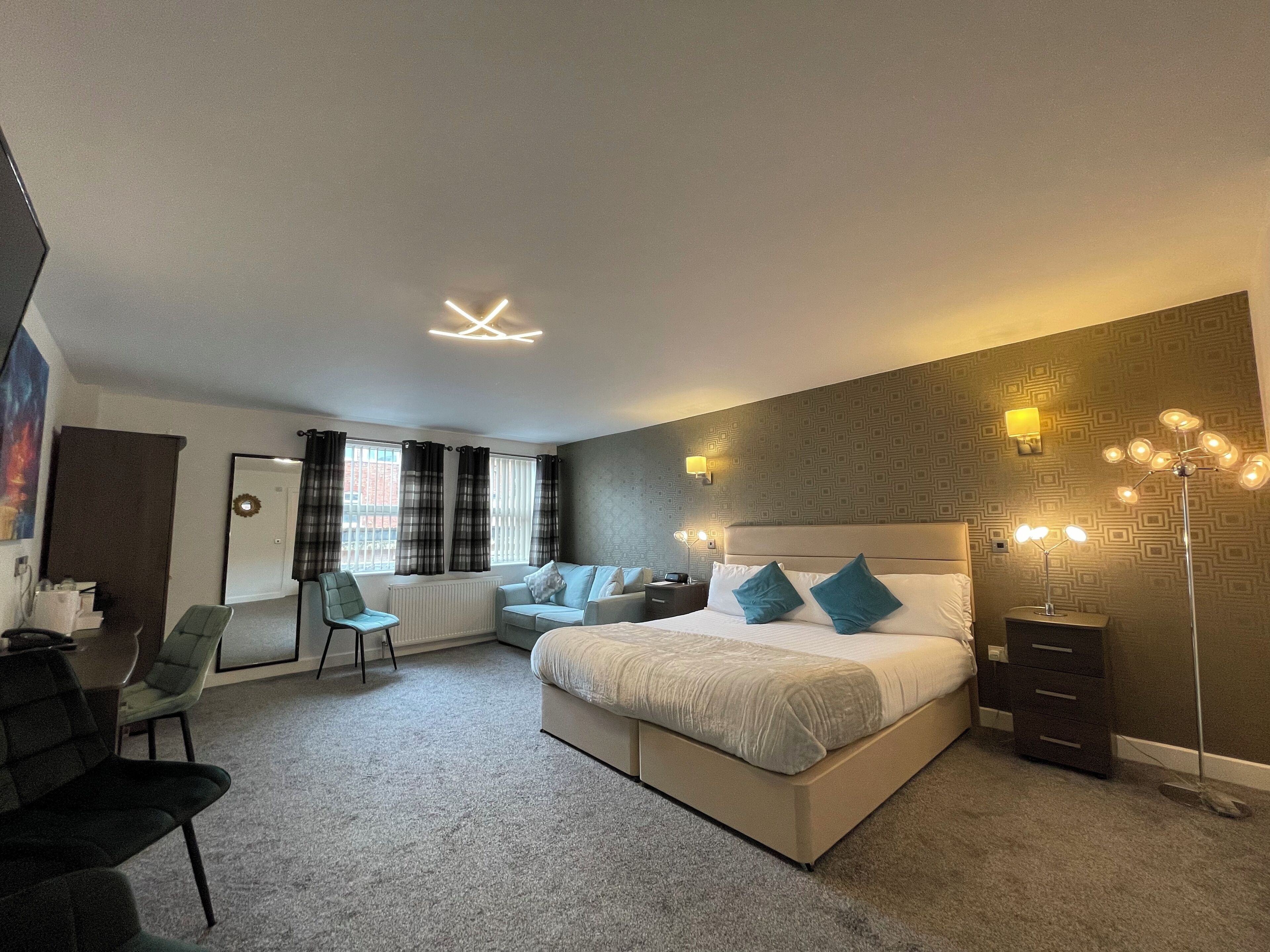 A modern hotel room with a large bed, a desk, a chair, and a wardrobe.