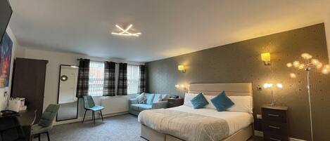 A modern hotel room with a large bed, a desk, a chair, and a wardrobe.