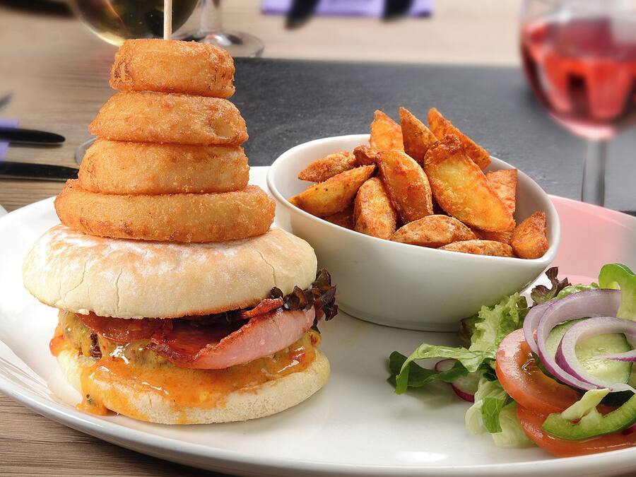 Un sándwich con una torre de alimentos fritos, un bol de papas fritas y una ensalada.
