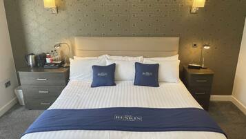 A hotel room with a bed, two nightstands, a lamp, a coffee maker, and a suitcase.