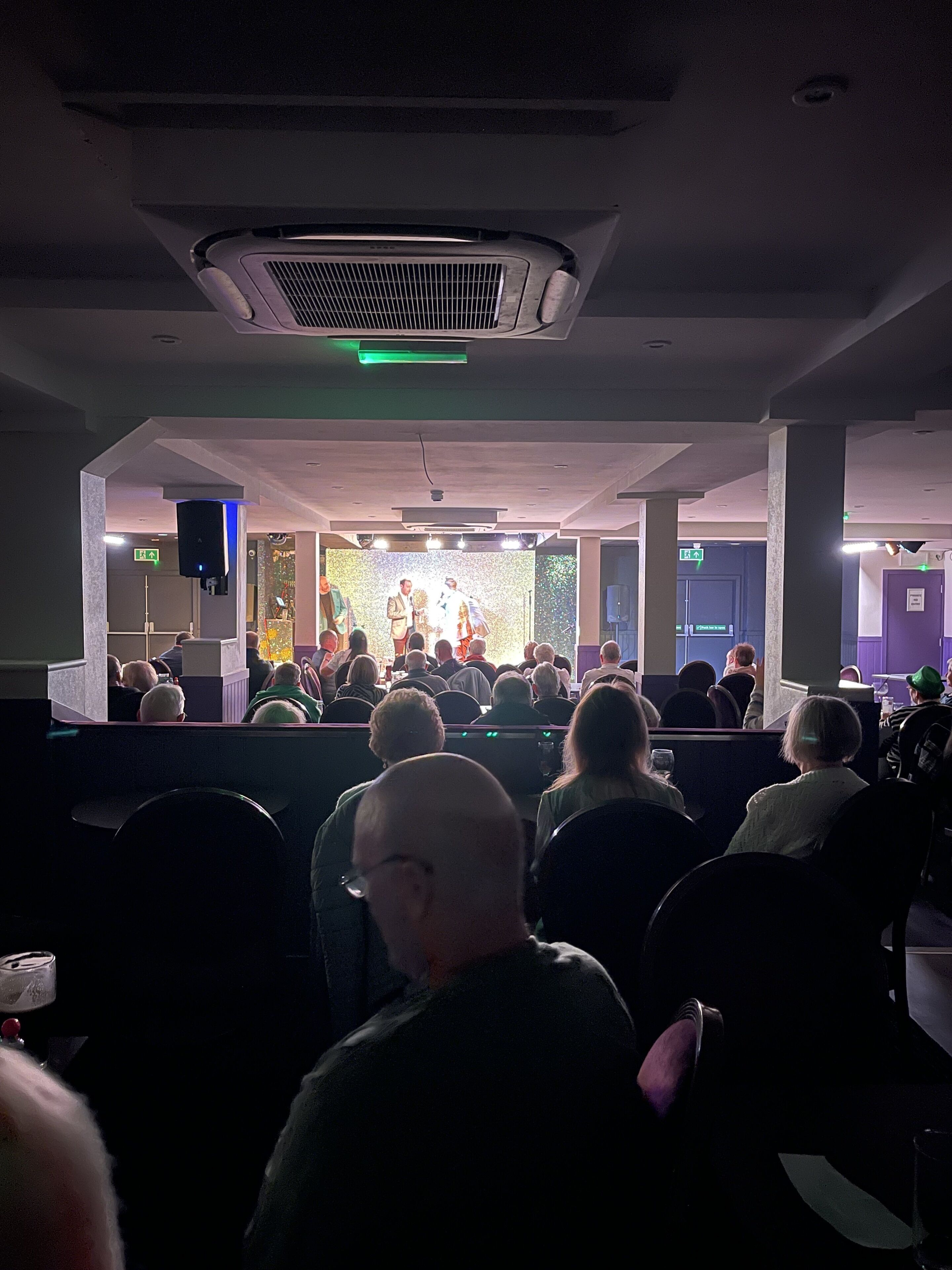 A conference room with a stage, rows of chairs, and a ceiling air conditioning unit.