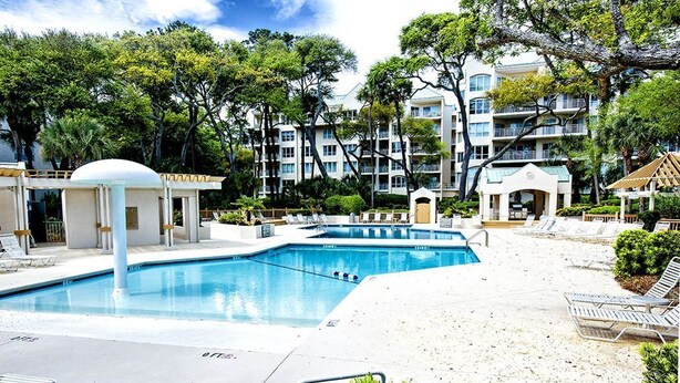 A swimming pool with lounge chairs, a covered area, and a building with multiple balconies in the background. - Sunset Escape 2 Bedroom Holiday Home (Hilton Head Island)