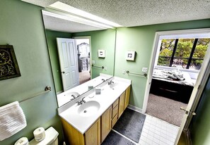 A bathroom with a double sink, a toilet, and a mirror. There is a towel rack and a door leading to a bedroom. - Sunset Escape 2 Bedroom Holiday Home (Hilton Head Island)
