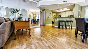 A spacious living area with a wooden floor, a sofa, a coffee table, and a kitchen area with a bar stool. - Sunset Escape 2 Bedroom Holiday Home (Hilton Head Island)