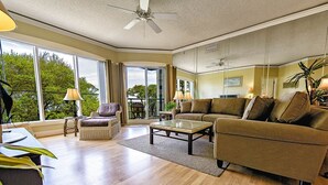 A spacious living room with a large window, a ceiling fan, and a sofa set. - Sunset Escape 2 Bedroom Holiday Home (Hilton Head Island)