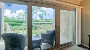 Habitación con puerta de vidrio corredera que da a un balcón con mobiliario de mimbre y vistas a un jardín ajardinado.