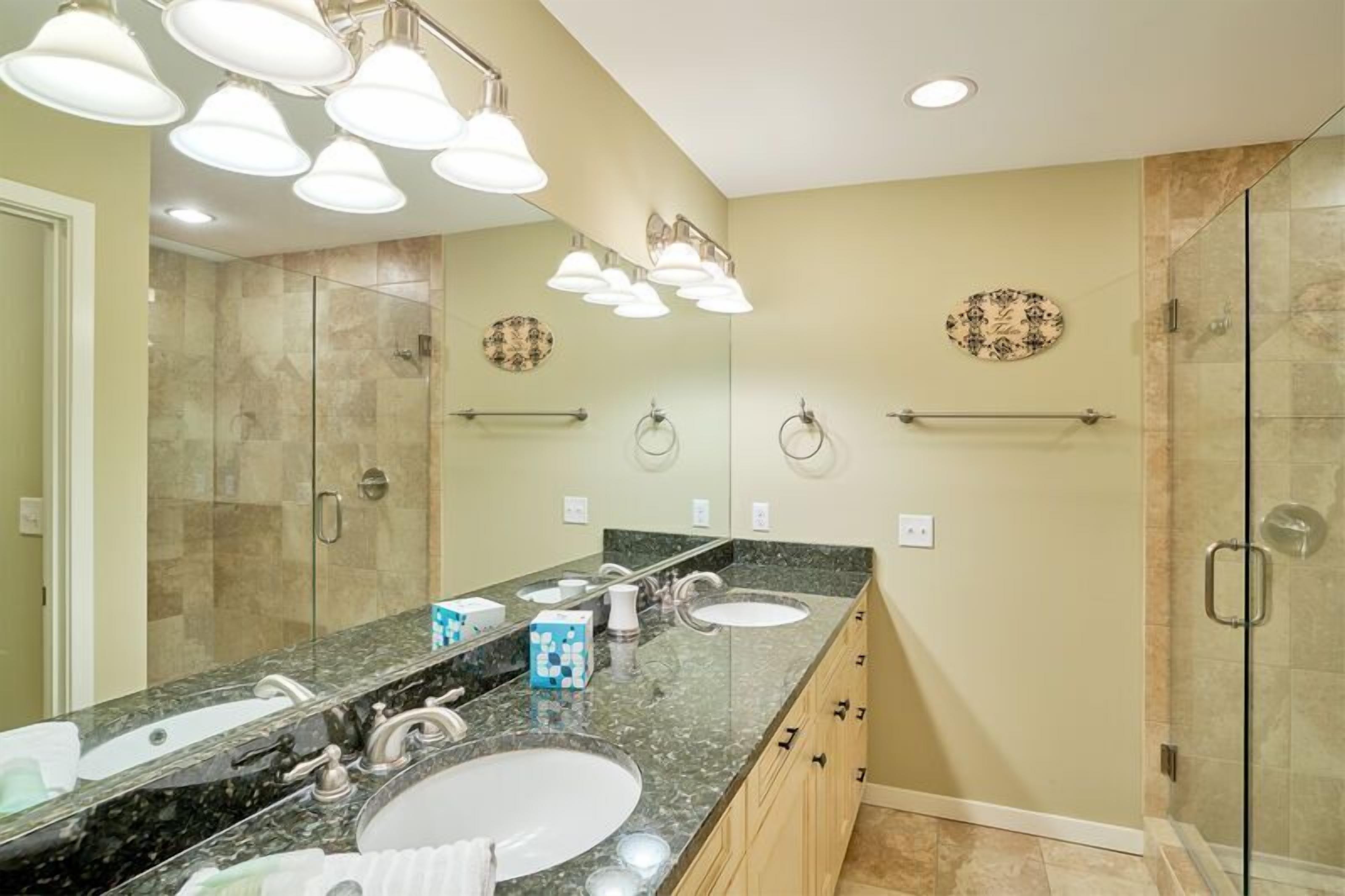 A modern bathroom with a large mirror, two sinks, and a glass shower enclosure.