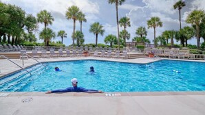 Una piscina con sillones de descanso y palmeras.