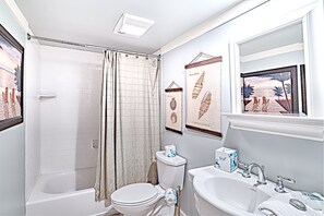 A bathroom with a shower, toilet, sink, and framed artwork on the wall. - Vista Verde 2 Bedroom Holiday Home (Hilton Head Island)