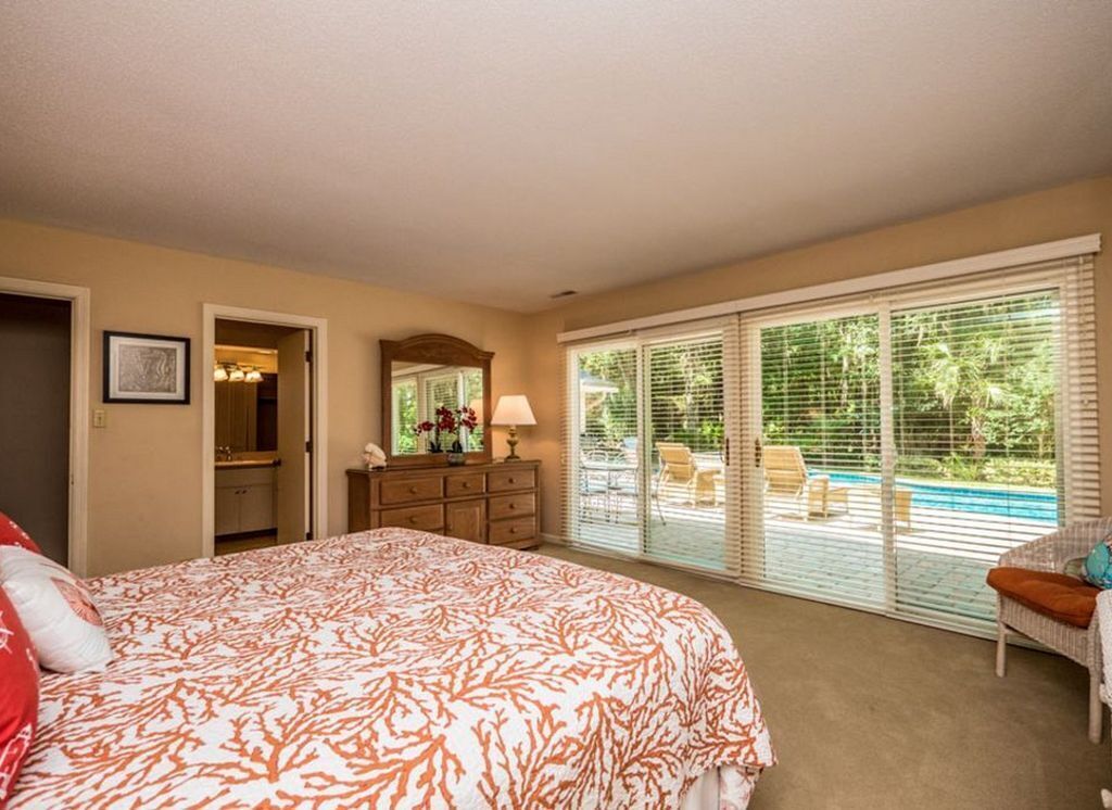 Un dormitorio con una cama grande, un aparador, un espejo y vistas a una piscina a través de puertas correderas de cristal.