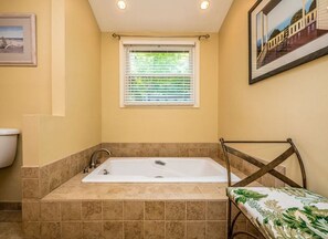 A bathroom with a bathtub, a window with blinds, and a framed picture on the wall.