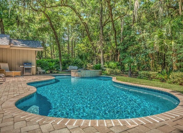 A swimming pool with a curved edge, surrounded by a brick patio.