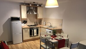 Cozinha compacta com forno embutido, micro-ondas e fogão a gás. Há uma mesa de jantar com cadeiras e um pequeno vaso de planta.
