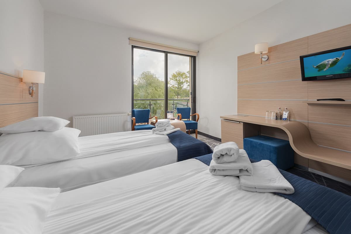 Une chambre d’hôtel avec deux lits, une télévision, un bureau et un balcon équipé de chaises.
