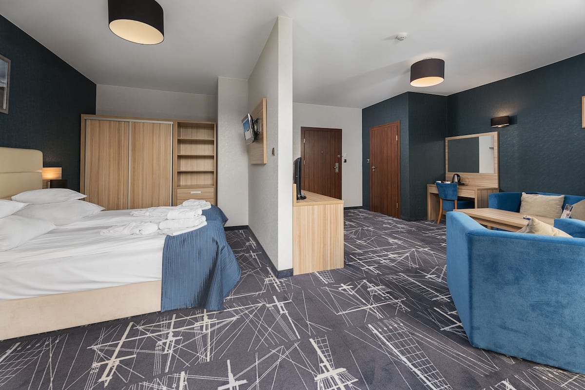 Une chambre d’hôtel moderne avec un lit, un canapé bleu, une armoire en bois, un bureau et un miroir.