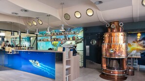 Un espace bar doté d’un grand poêle en cuivre, d’étagères remplies de bouteilles d’alcool et d’une fresque représentant un bateau sur le mur.
