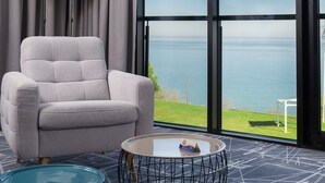 Une chambre moderne avec un fauteuil gris, une table basse en verre et une grande fenêtre donnant sur la mer.