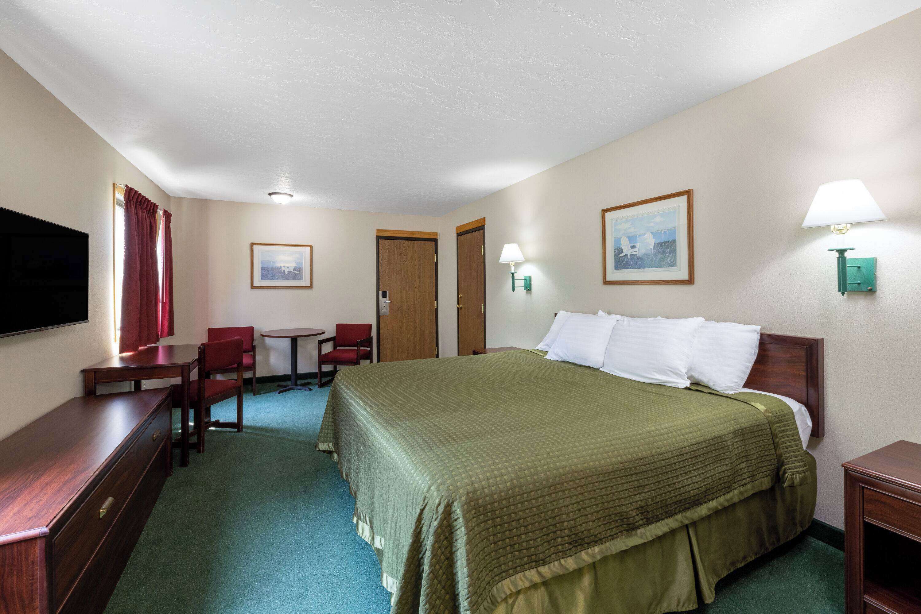 Une chambre d’hôtel avec un grand lit, un bureau, une chaise, une petite table et deux lampes.