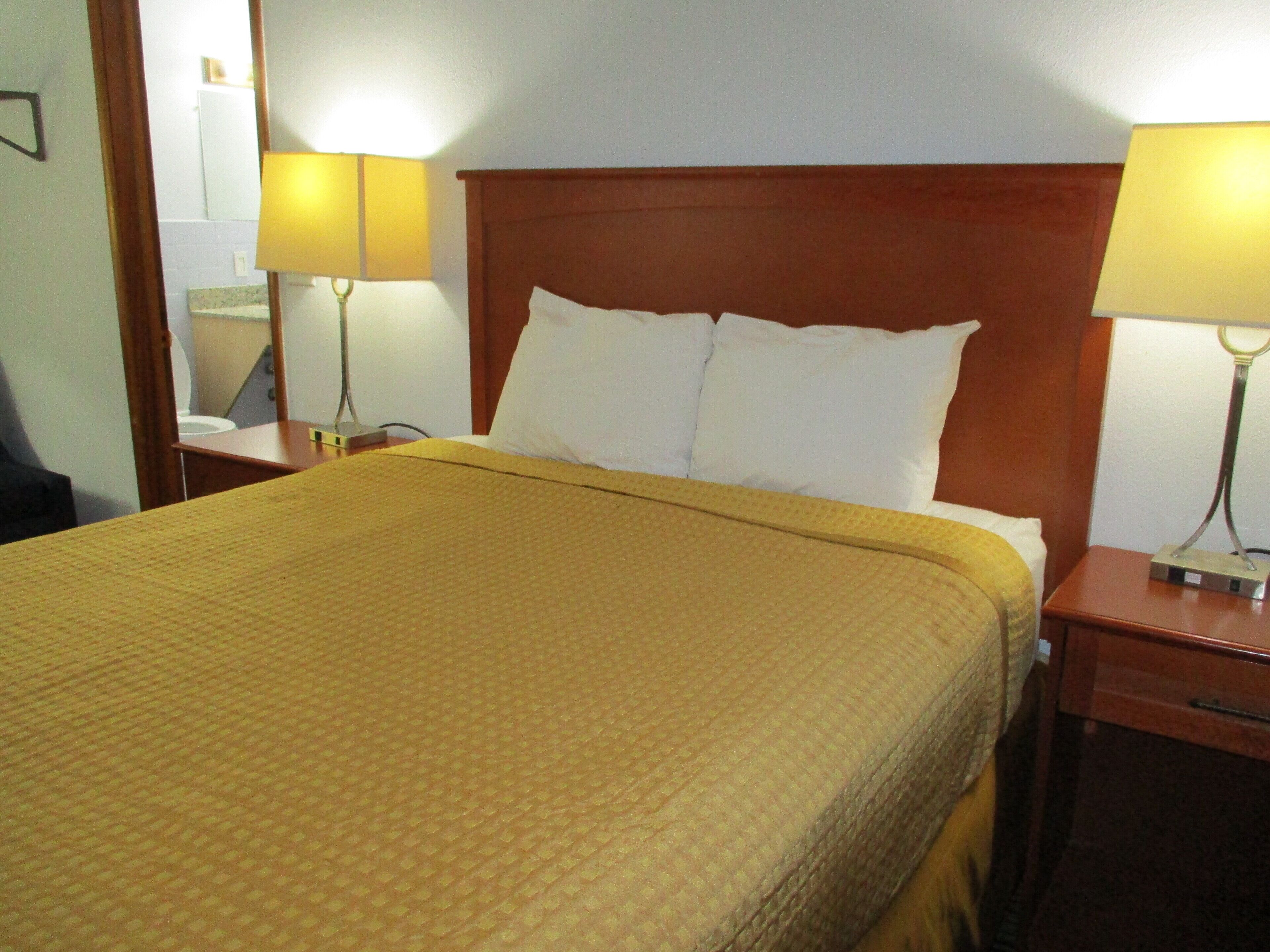 Une chambre d’hôtel avec un grand lit, deux lampes de chevet, une tête de lit en bois et une table de chevet avec une lampe.
