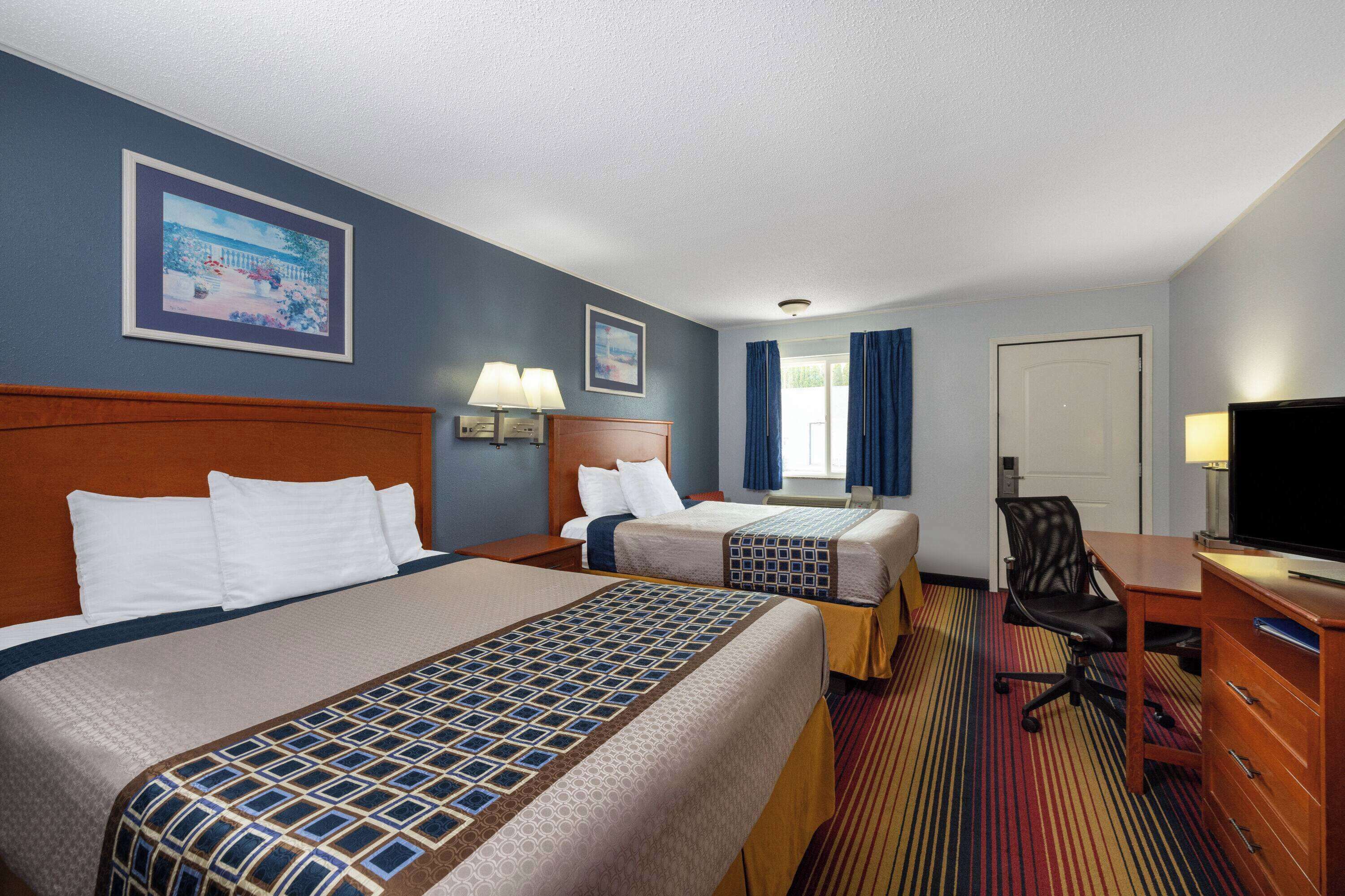 Une chambre d’hôtel avec deux lits, un bureau, une chaise, une télévision et une fenêtre avec des rideaux.