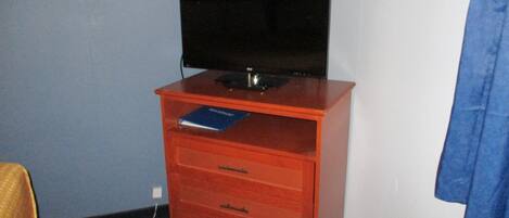 Una habitación pequeña con un mueble de madera que contiene un televisor, un libro y un aire acondicionado blanco.