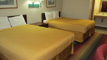 Una habitación de hotel con dos camas, alfombra a rayas y un baño con espejo y lavamanos.