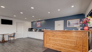 A reception area with a wooden desk, a white door, a framed picture on the wall, and a small table with chairs. - Travelodge by Wyndham Spirit Lake/Okoboji (Spirit Lake)