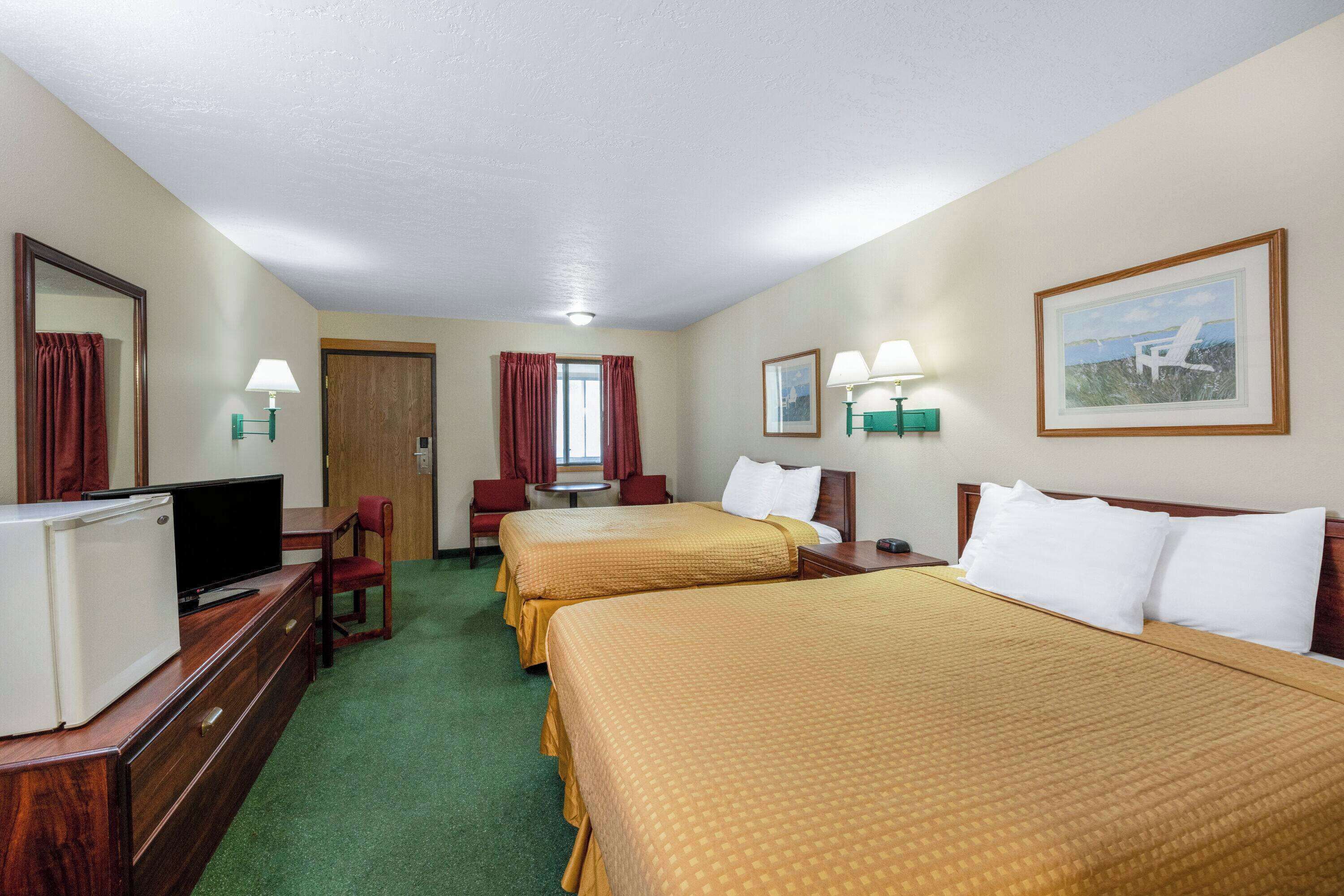 A hotel room with two beds, a television, a desk, and a chair.