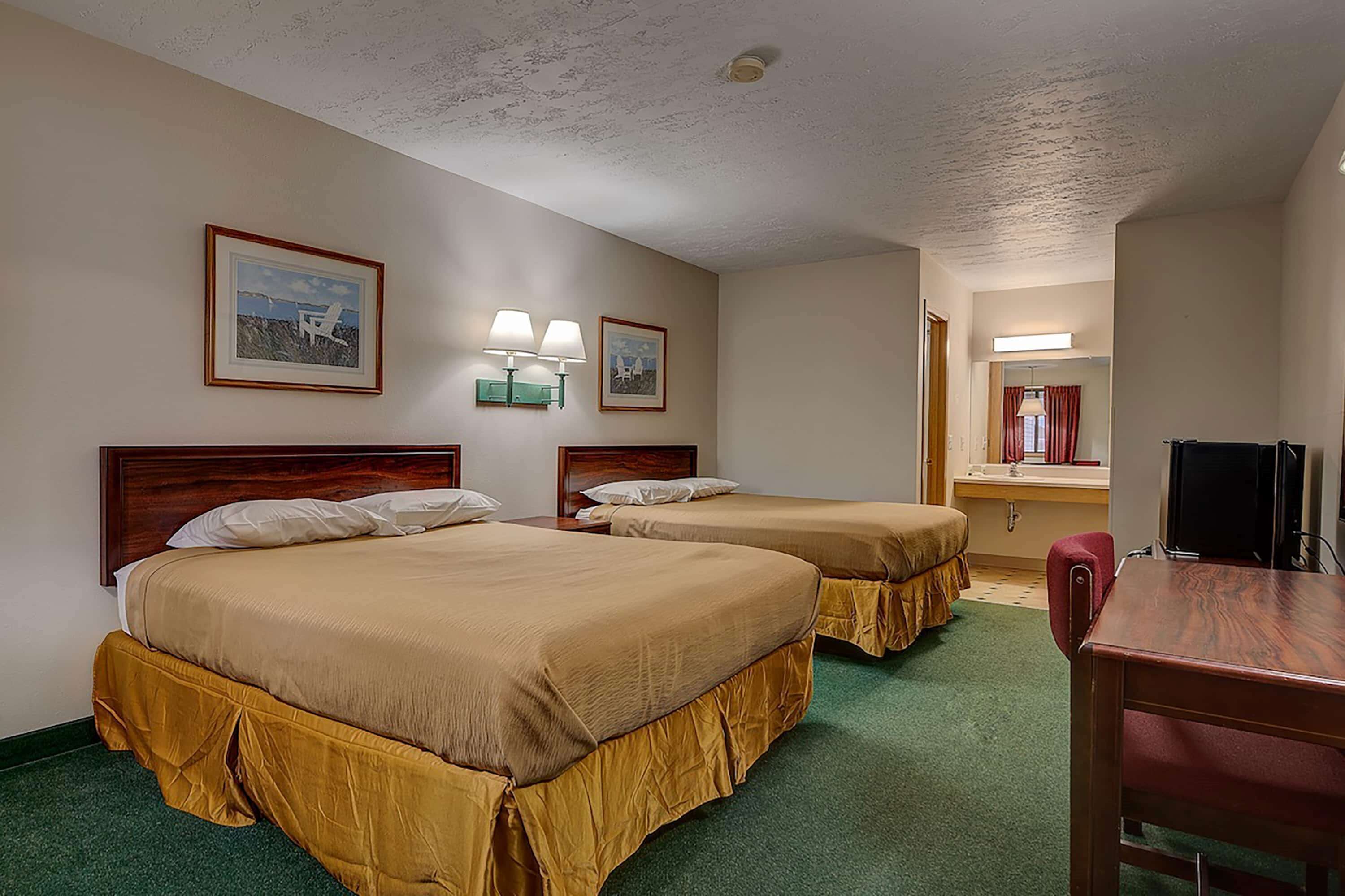 A hotel room with two beds, a desk, a chair, and a television.