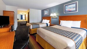 A hotel room with two beds, a desk with a TV, a chair, and a bathroom visible through an open door. - Travelodge by Wyndham Spirit Lake/Okoboji (Spirit Lake)