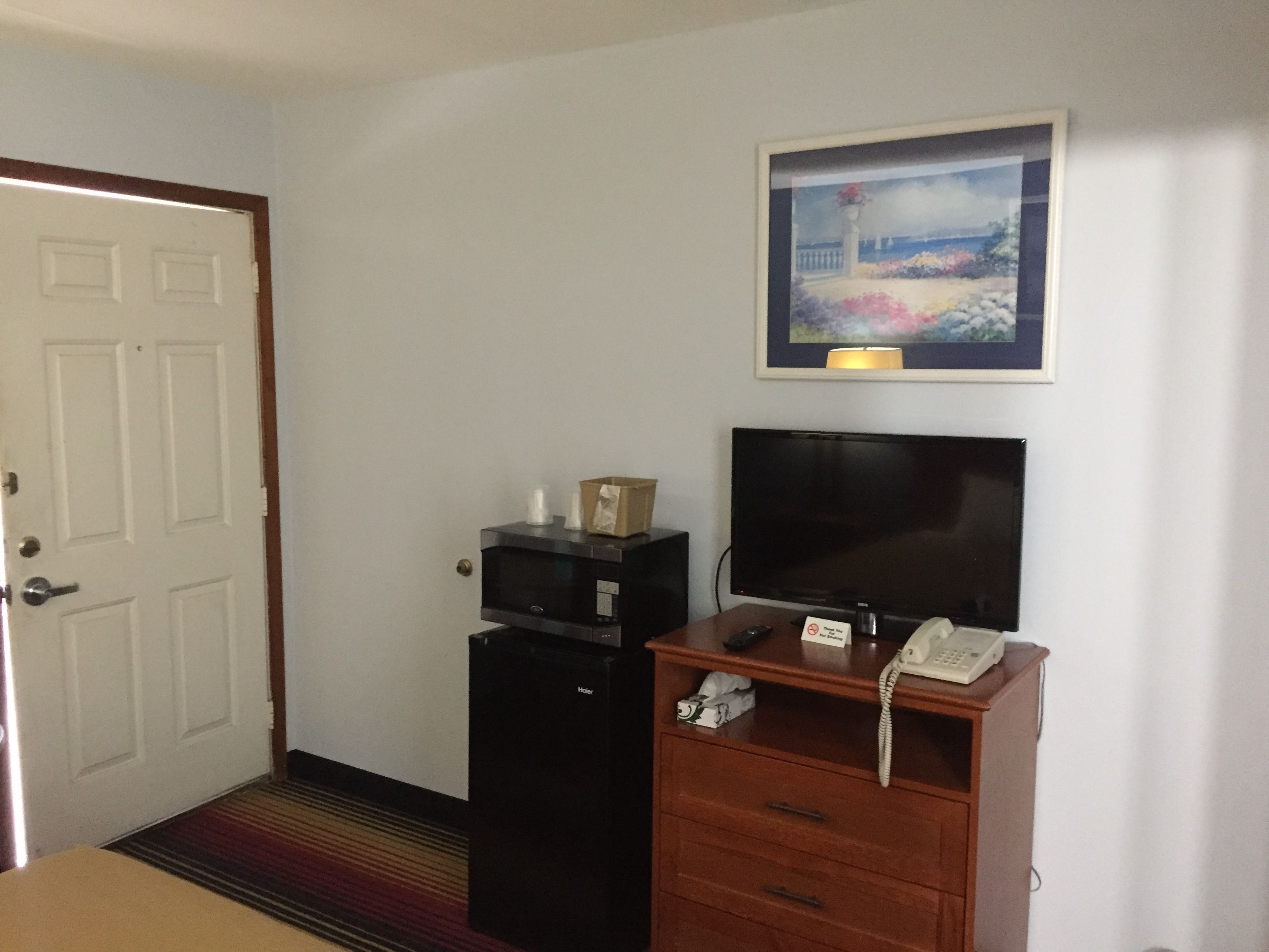 Habitación de hotel con puerta, escritorio con televisor, teléfono y un cuadro en la pared.