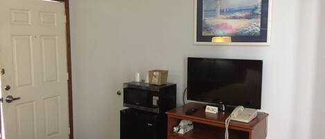 Habitación de hotel con puerta, escritorio con televisor, teléfono y un cuadro en la pared.