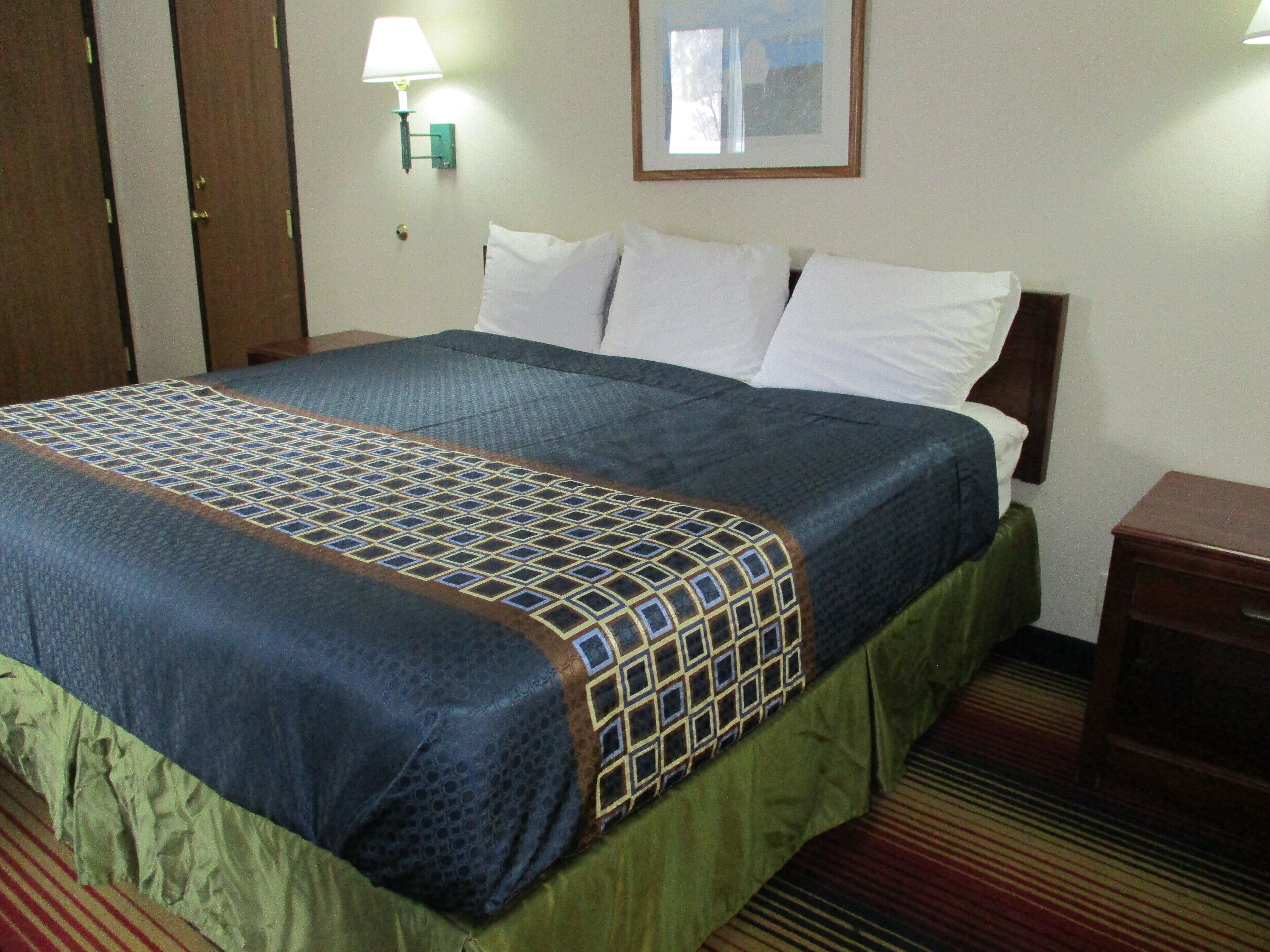 Una habitación de hotel con una cama, una mesita de noche, una lámpara y un cuadro en la pared.