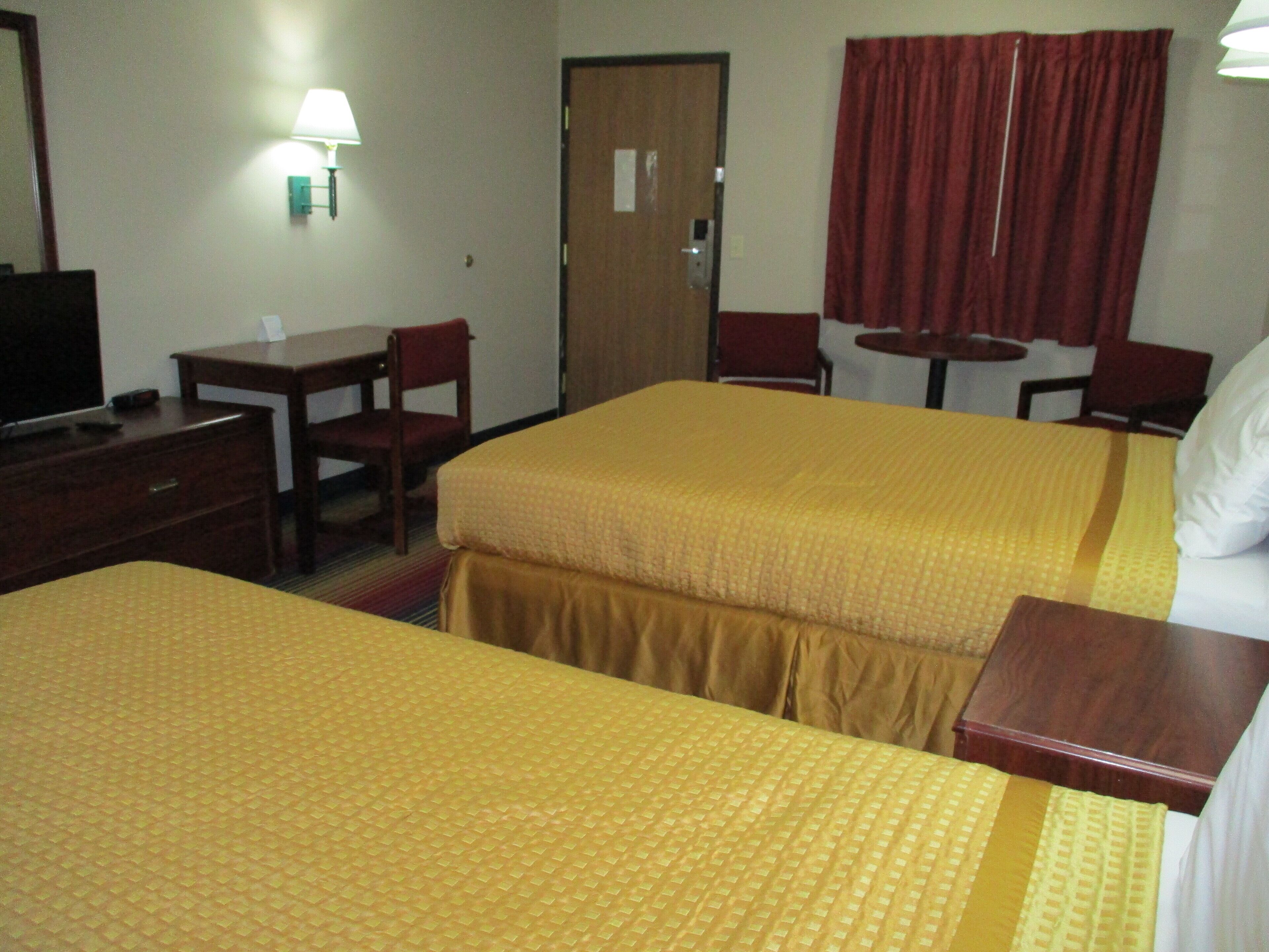 A hotel room with two beds, a desk, a chair, a TV, and a lamp.